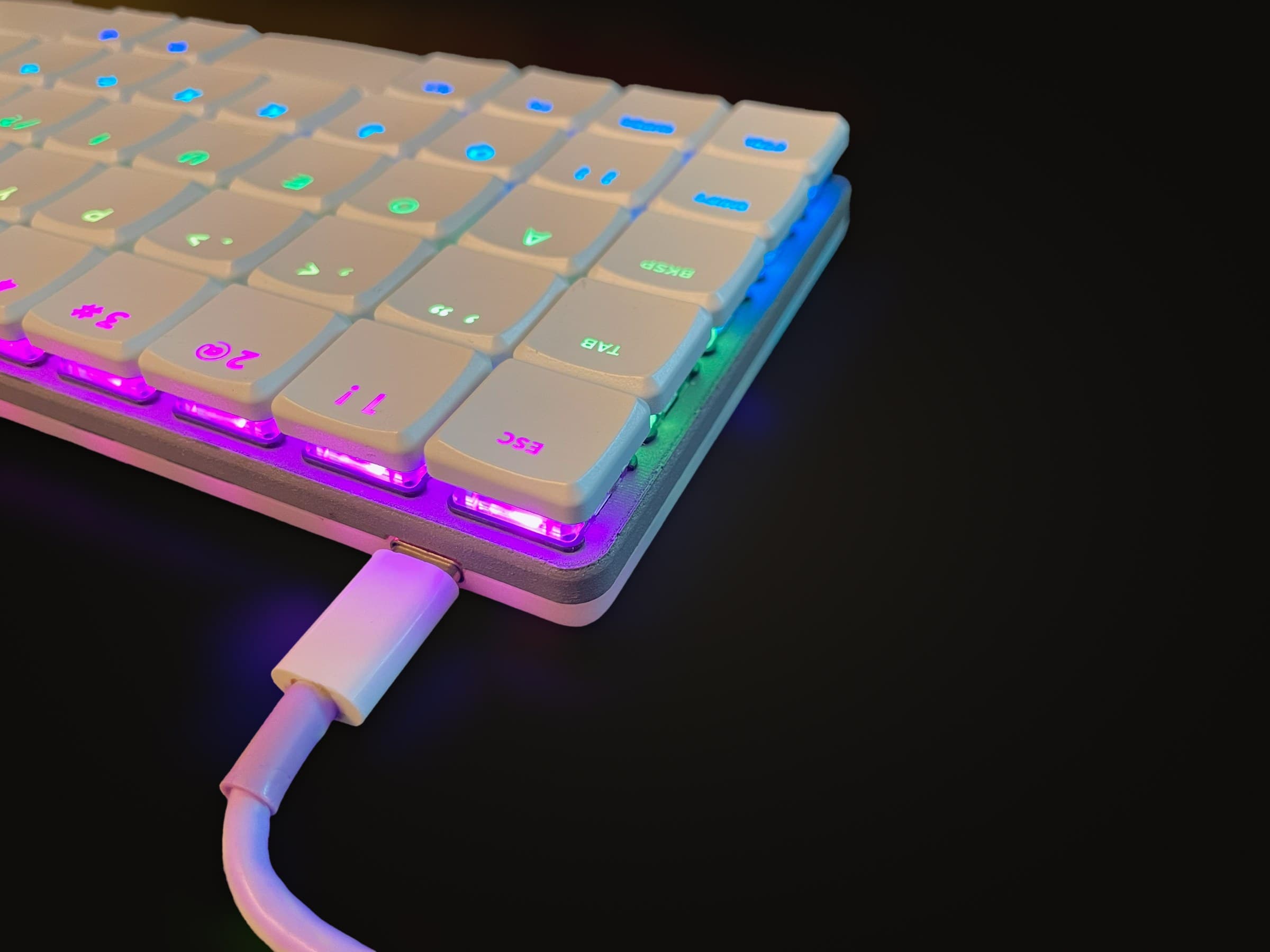 KeBe v1 lit in a rainbow, a white USB-C cable plugged into its back edge.